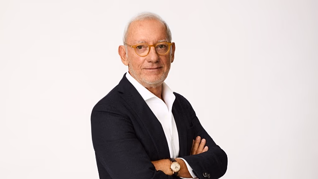 un señor mayor con pelo blanco y gafas redondas, vestido de traje